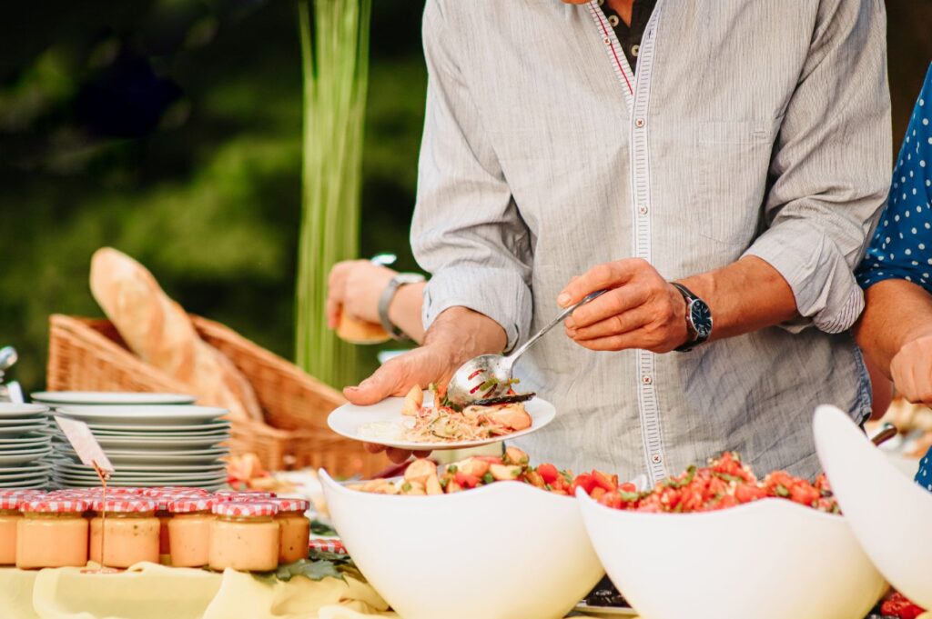 Ein Foto von einem Mann wie er Salat, von einem Buffet mit diversen Speisen, auf seinen Teller löffelt
