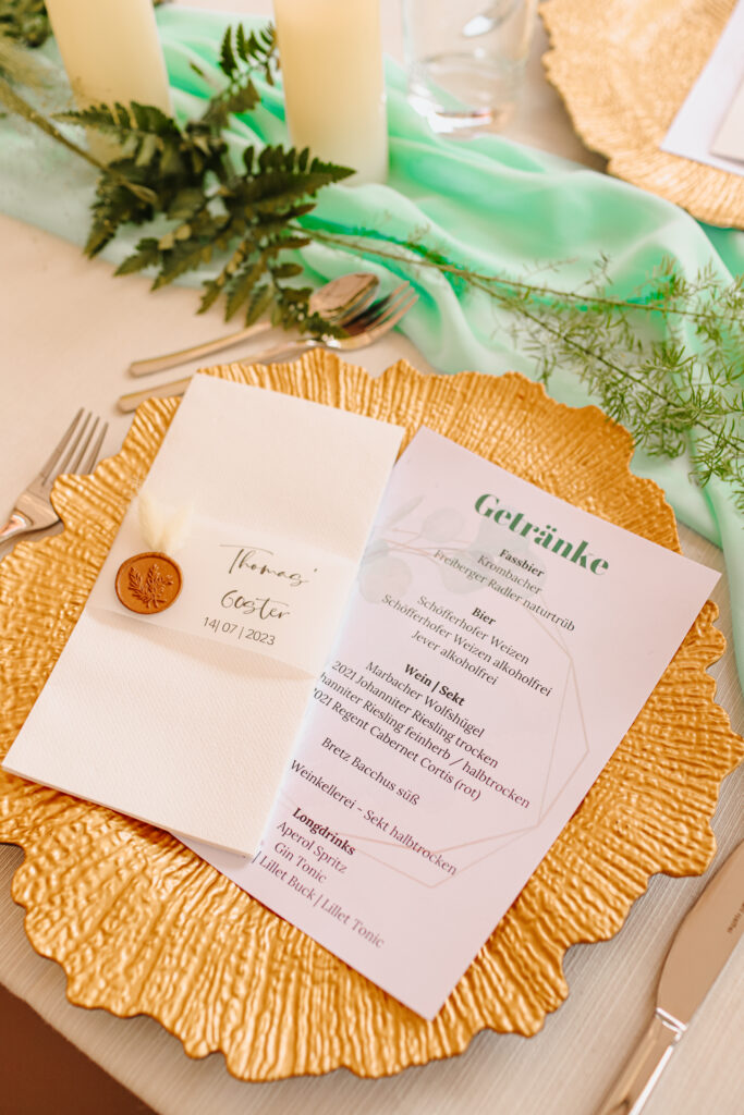 Elegant gedeckter Hochzeitstisch mit Getränkekarte, goldener Platzteller und Namenskarte